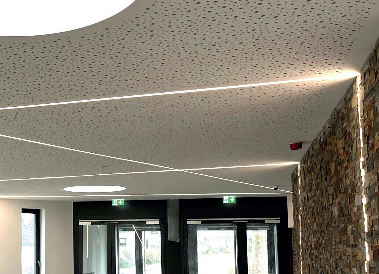 Modernes Interieur mit perforierter Decke und LED-Lichtbändern, daneben eine Wand aus Steinfliesen und Glastüren.